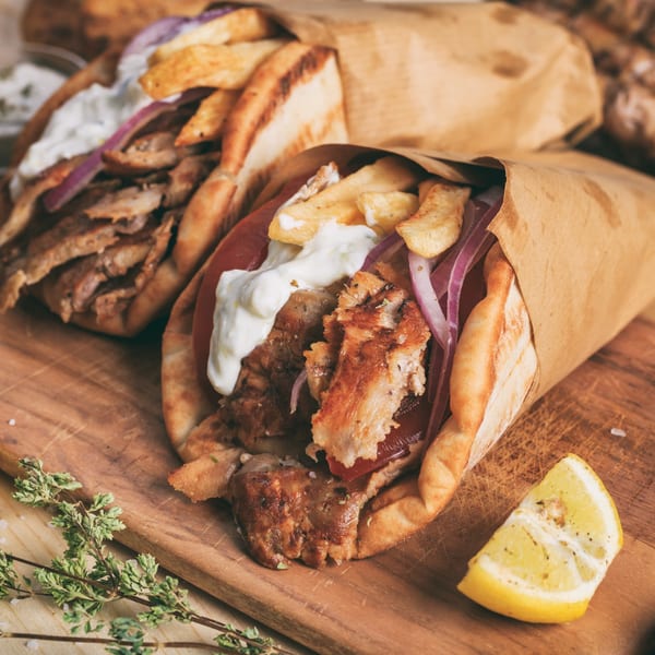 Two Greek souvlaki gyros with meat, fries, tzatziki, and red onion on a wooden board.