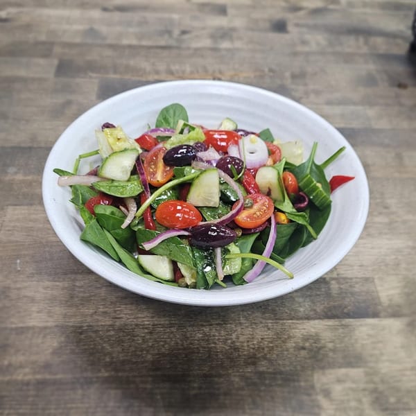 A vibrant Greek salad in a white bowl, featuring spinach, tomatoes, cucumbers, red onions, and olives.