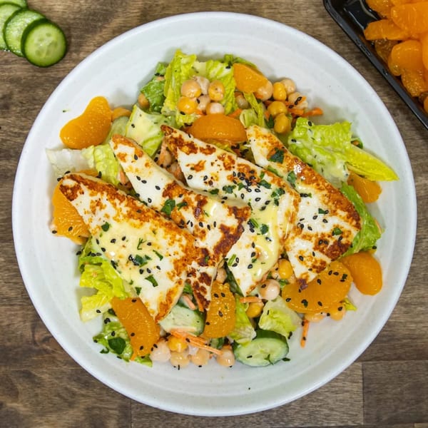 A Greek salad with grilled halloumi cheese, chickpeas, lettuce, cucumber, and orange segments.