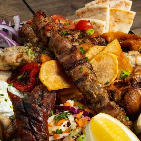 A platter of grilled Greek meats, including skewers, with pita bread, fries, and salad.
