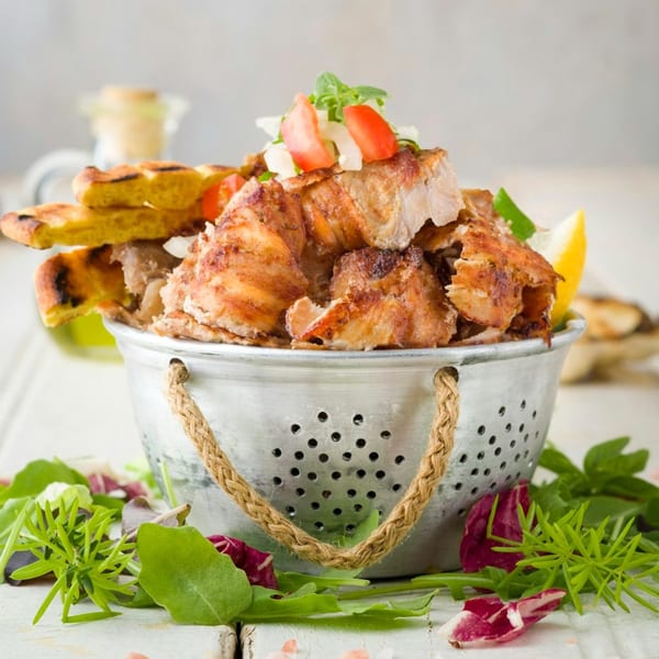 Greek chicken gyros with pita bread, tomatoes, and herbs in a metal colander.