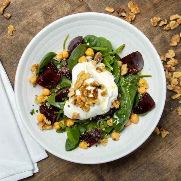 A Greek salad with spinach, beets, chickpeas, and walnuts, topped with a dollop of yogurt.