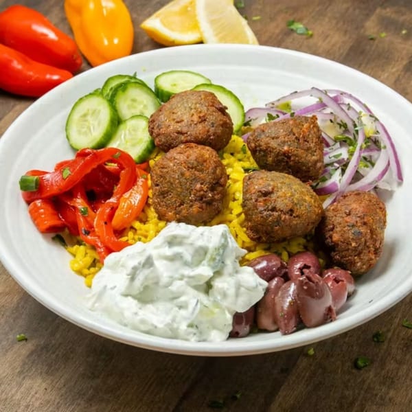 A Souvlaqueria falafel bowl with yellow rice, tzatziki, olives, cucumbers, red peppers, and red onions.