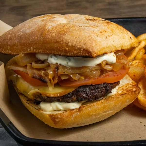 Souvlaqueria's burger with grilled onions, tomatoes, cheese, and tzatziki sauce, served with fries.