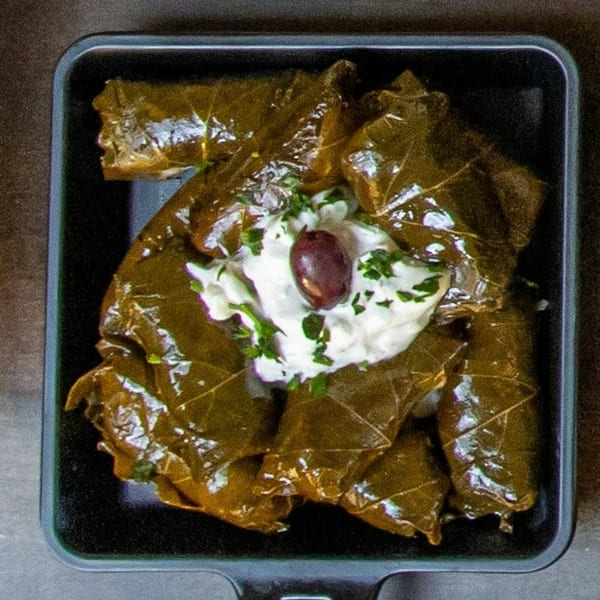 A black tray filled with Souvlaqueria's dolmades, topped with yogurt, fresh herbs, and an olive.