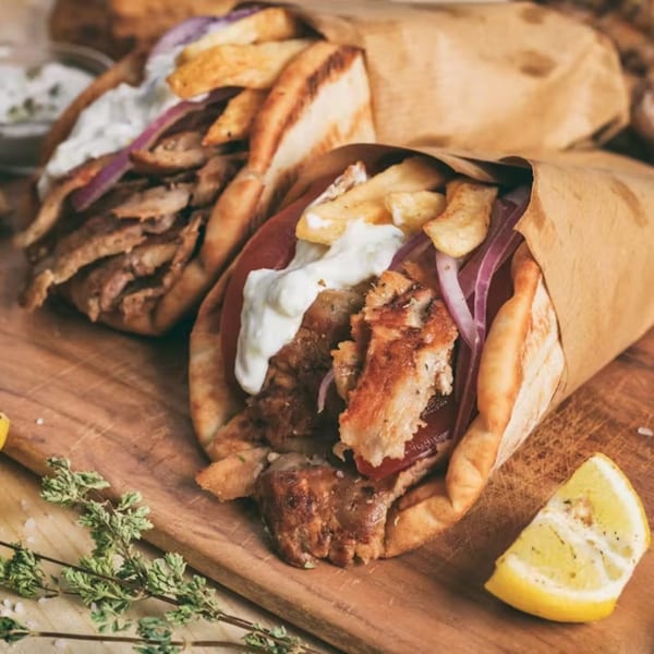 Two Greek gyros, filled with meat, fries, red onion, and tzatziki, on a wooden board.