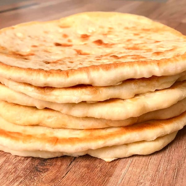 Stack of five golden-brown Souvlaqueria pita breads on a wooden surface.