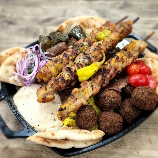 Souvlaqueria's Greek platter with chicken skewers, falafel, pita, hummus, dolmades, and cherry tomatoes.