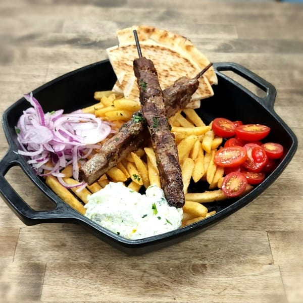 Souvlaqueria's Greek kebab plate with fries, pita, tzatziki, red onions, and cherry tomatoes.