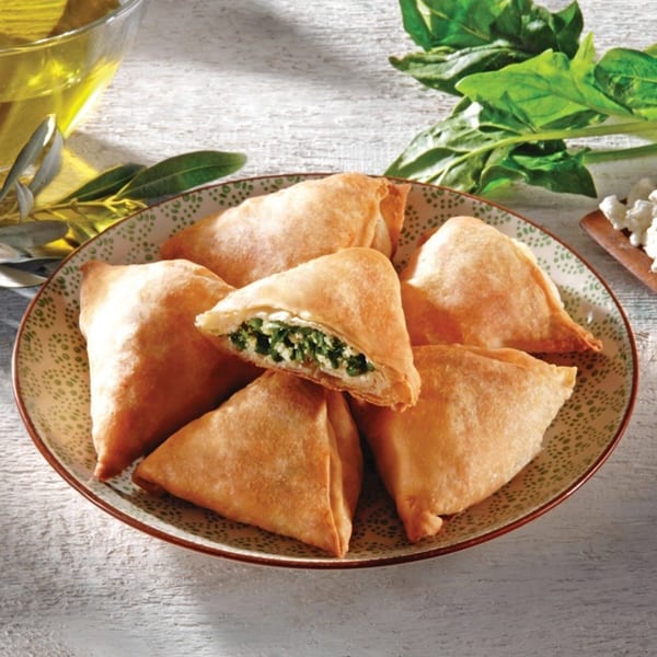 A plate of golden-brown Greek spanakopita pastries, one cut open to show spinach and feta filling.