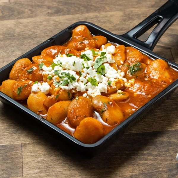 Greek potatoes in a black pan, topped with feta cheese and parsley, on a wooden table.