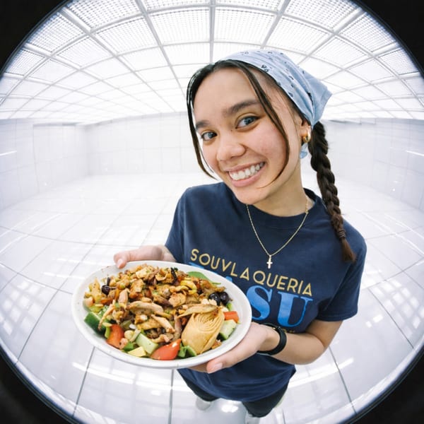 Smiling woman in a Souvlaqueria shirt holding a Greek salad with chicken, artichoke, and olives.