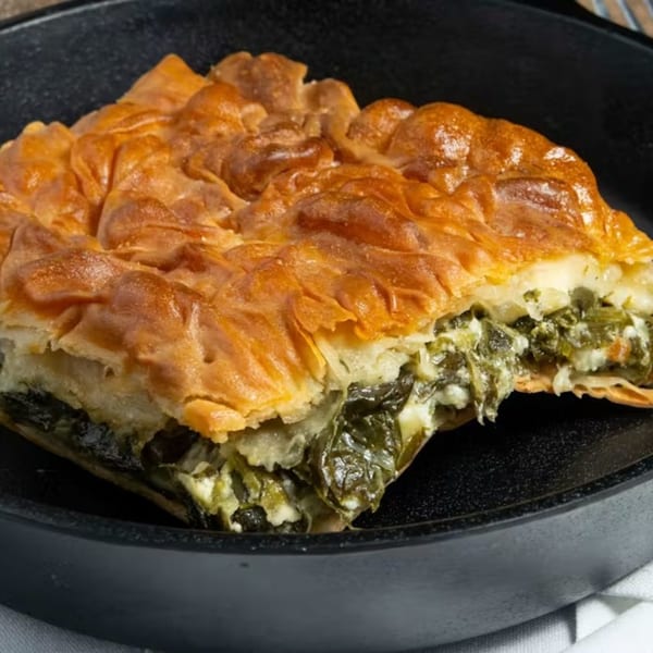 A golden-brown slice of spanakopita, a Greek spinach and feta pie, in a black pan.