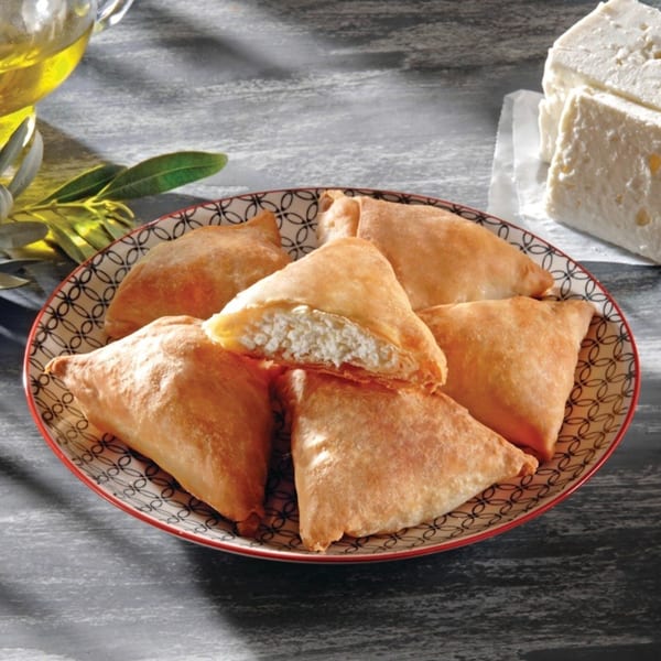 A plate of golden-brown, triangular Greek cheese pastries, one cut open to show the creamy filling.