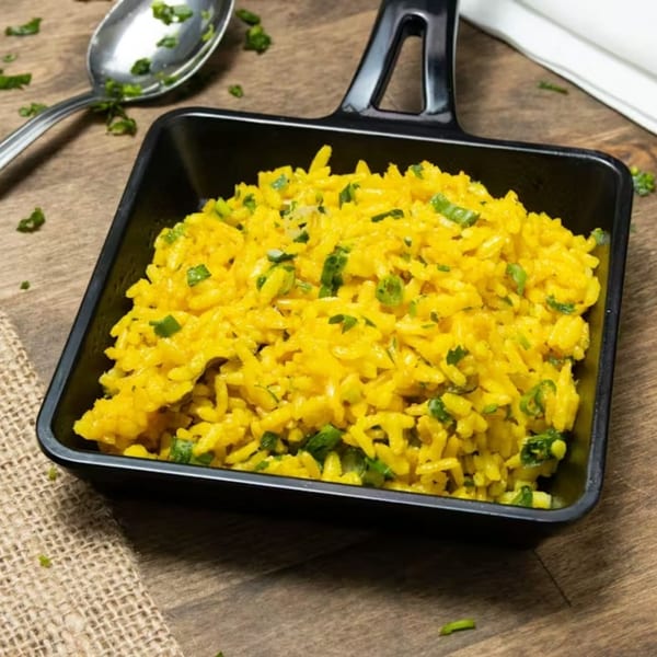 Bright yellow Greek rice pilaf with green herbs in a black serving dish on a wooden table.