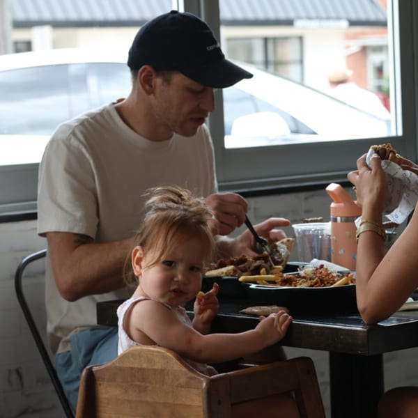 A family enjoying Greek food at Souvlaqueria, with a toddler in a high chair.