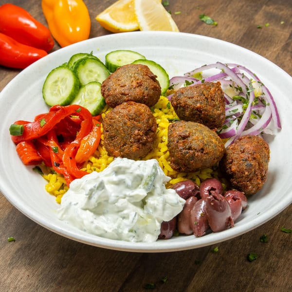 A Souvlaqueria falafel bowl with yellow rice, cucumbers, red peppers, tzatziki, olives, and red onions.