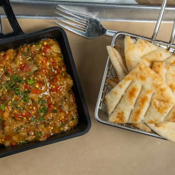 Greek eggplant dip with red peppers and herbs, served with pita bread in a metal basket.