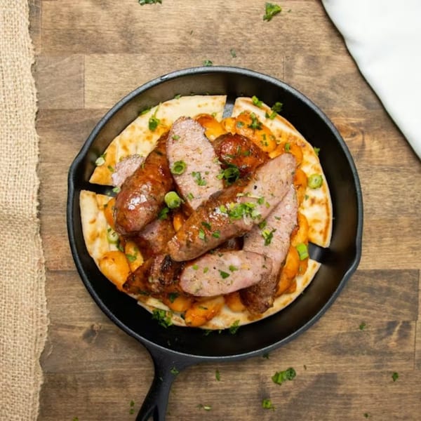 Souvlaqueria's Greek sausage with beans and pita bread in a cast iron pan.
