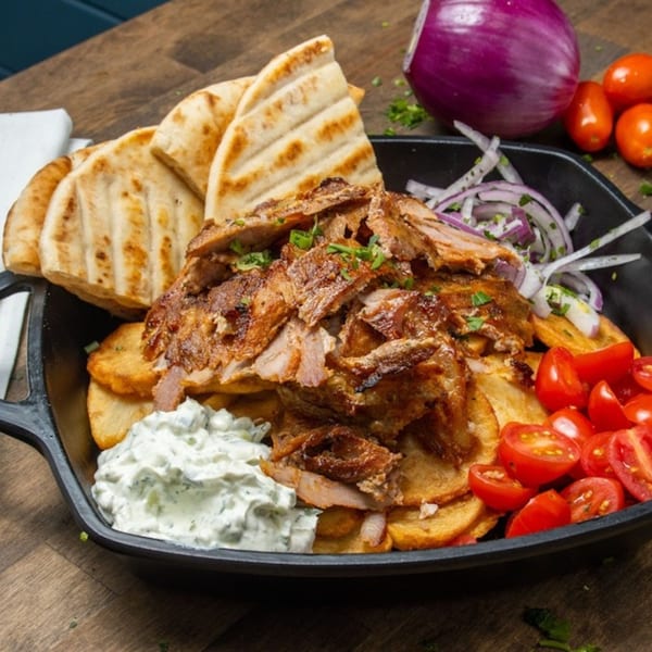 Souvlaqueria's Greek gyro platter with sliced meat, pita, fries, tzatziki, tomatoes, and red onion.